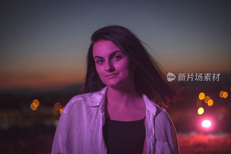 Close up portrait of happy young woman at night, she is lit by purple lights
